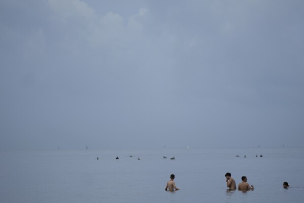 FILE - People swim in the ocean off of Crandon Park, July 28, 2023, in Key Biscayne, Fla. At about summer's halfway point, the record-breaking heat and weather extremes are both unprecedented and unsurprising, hellish yet boring in some ways, scientists say. (AP Photo/Rebecca Blackwell, File)