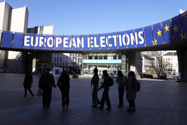 FILE - A group stands under an election banner outside the European Parliament in Brussels on April 29, 2024. The European Union marks Europe Day on Thursday, May 9, but instead of the traditionally muted celebrations, all eyes are on the EU elections in one month time which portend a steep rise of the extreme right and a possible move away from its global trendsetting climate policies. (AP Photo/Virginia Mayo, File)