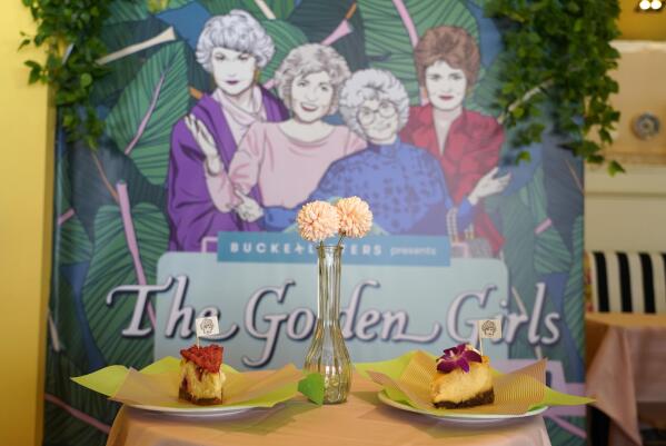 Cheesecake dessert items are pictured in front of a portrait of "The Golden Girls" cast at the Golden Girls Kitchen pop-up restaurant, Monday, July 25, 2022, in Beverly Hills, Calif. The pop-up only has reservations through the end of October. But there are plans to take it on the road to New York, Chicago, San Francisco and Miami. (AP Photo/Chris Pizzello)