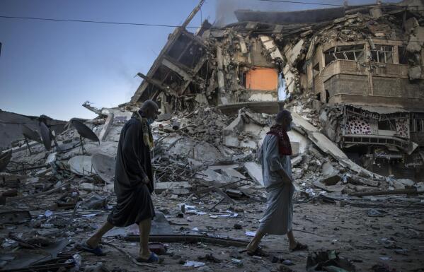 Palestinians walk next to the remains of a destroyed 15 story building after being hit by Israeli airstrikes on Gaza City, Thursday, May 13, 2021. (AP Photo/Khalil Hamra)