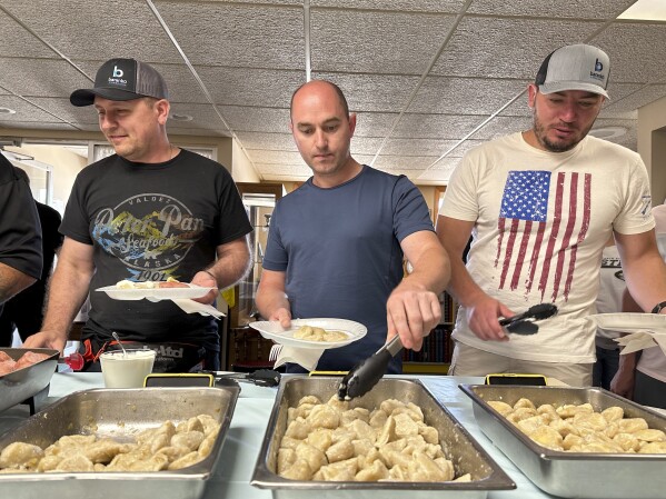 Maksym Bunchukov, Andrii Hryshchuk and Ivan Sakivskyi help themselves to perogies at a lunch hosted Monday, July 17, 2023, by the Ukrainian Cultural Institute in Dickinson, North Dakota. The three Ukrainians are among the first recruits of the North Dakota Petroleum Council's Bakken Global Recruitment of Oilfield Workers program. (AP Photo/Jack Dura)