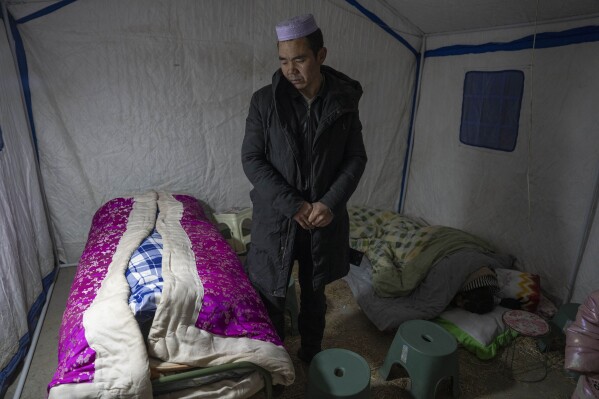Ma Lianqiang looks over at the body of his wife Han Suofeiya who was killed in an earthquake as his daughter sleeps nearby in Yangwa village near Dahejia town in northwestern China's Gansu province, Wednesday, Dec. 20, 2023. (AP Photo/Ng Han Guan)