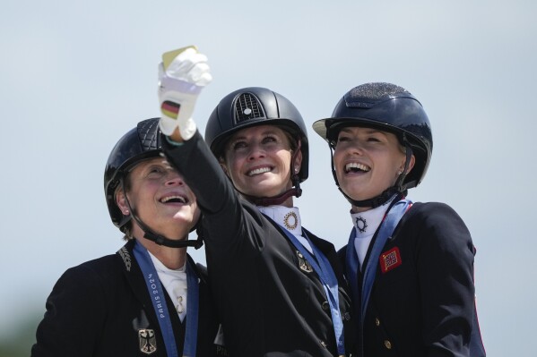 Medalists from left to right, Germany's Isabell Werth, Jessica von Bredow-Werndl and Britain's Charlotte Fry take a selfie to celebrate their silver, gold and bronze medals at the dressage Individual Grand Prix Freestyle, at the 2024 Summer Olympics, Sunday, Aug. 4, 2024, in Versailles, France. (AP Photo/Mosa'ab Elshamy)