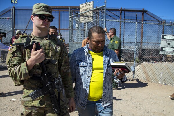 FILE - Migrants are escorted by a U.S. Army soldier after entering into El Paso, Texas from Ciudad Juarez, Mexico to be processed by immigration authorities, May 10, 2023. The Pentagon is pulling 1,100 active duty troops from the U.S.-Mexico border it deployed earlier this year as the government prepares for the end of asylum restrictions linked to the pandemic. (AP Photo/Andres Leighton, File)
