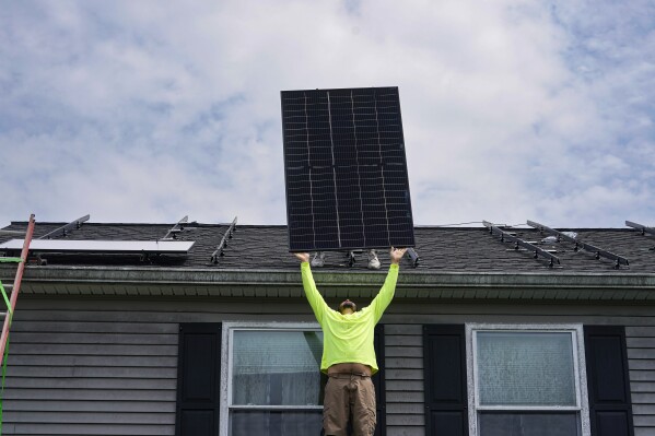 Nicholas Hartnett, owner of Pure Power Solar, lifts a solar panel to the roof of a home in Frankfort, Ky., Monday, July 17, 2023. Since passage of the Inflation Reduction Act, it has boosted the U.S. transition to renewable energy, accelerated green domestic manufacturing, and made it more affordable for consumers to make climate-friendly purchases, such as installing solar panels on their roofs. (AP Photo/Michael Conroy)