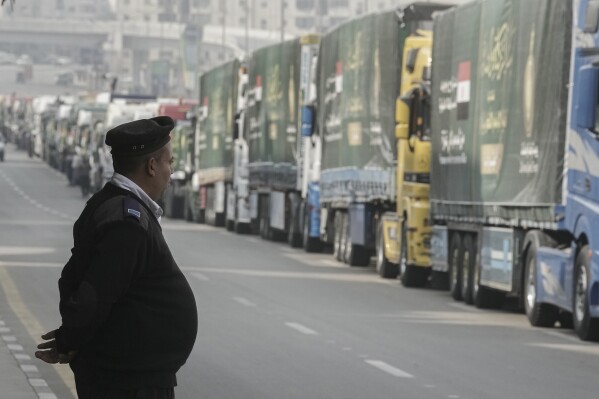 An Egyptian policeman stands in front of trucks of humanitarian aid at a parking point in Cairo, Egypt, as they wait to travel to cross the Rafah border crossing between Egypt and the Gaza Strip, Sunday, Jan. 26, 2025. (AP Photo/Amr Nabil)