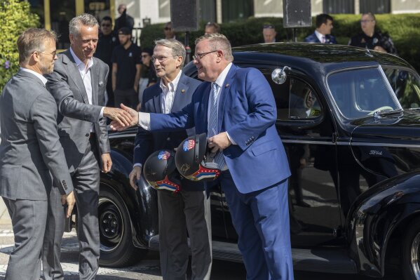 From left, Speedway Motorsports President and CEO Marcus Smith and NASCAR President Steve Phelps present Senate Majority Leader Paul Newton and House Speaker Tim Moore with vintage-style racing helmets during an announcement Thursday, Sept 28, 2023 outside the North Carolina Legislative Building in downtown Raleigh, N.C. The announcement was that the NASCAR All-Star Race will be held May 17-19 at the North Wilkesboro Speedway. (Travis Long/The News & Observer via AP)