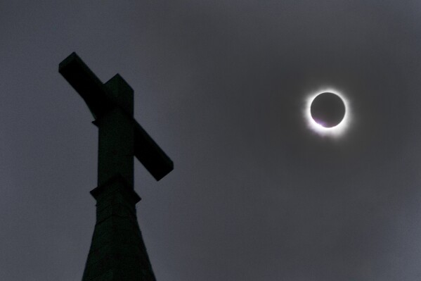 The moon partially covers the sun during a total solar eclipse, as seen below a cross atop the New Sweden Evangelical Lutheran Church steeple Monday, April 8, 2024, in Manor, Texas. (AP Photo/Charles Rex Arbogast)