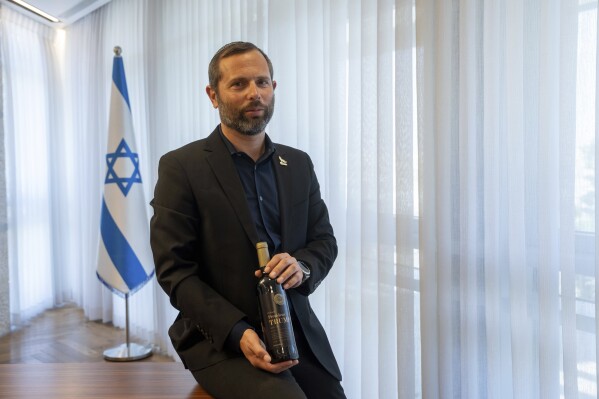 Israel Ganz, chairman of the Yesha settlers council and head of the Mateh Binyamin Regional Council, poses for a portrait holding a bottle of wine bearing the name of U.S. President-elect Donald Trump in the Shaar Binyamin Industrial Park in the West Bank, Monday, Nov. 11, 2024. (AP Photo/Ohad Zwigenberg)