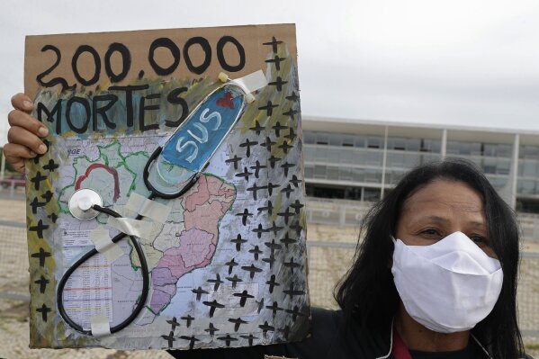 A protester holds a map of Brazil featuring a stethoscope and the Portuguese message "200,000 deaths" outside the presidential palace in Brasilia, Brazil, Friday, Jan. 8, 2021, the day after Brazil passed 200,000 COVID-19 deaths. (AP Photo/Eraldo Peres)
