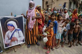 FILE - Homeless people gather beside a portrait of Saint Teresa, the founder of the Missionaries of Charity, to collect free food outside the order's headquarters in Kolkata, India, on Aug. 26, 2021. India’s government has allowed Mother Teresa’s charity to receive foreign funds, weeks after blocking it saying the Catholic organization did not meet conditions under local laws, a lawmaker said Saturday, Jan. 7, 2022.(AP Photo/Bikas Das, File)