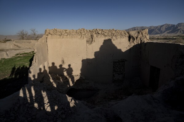People stand next to a house that destroyed by U.S. forces in a village in a remote region of Afghanistan, on Wednesday, Feb. 22, 2023. In a nearby village, a baby was orphaned during a similar U.S. raid in 2019. A Marine who adopted her claims her parents were foreign fighters. But villagers say they were innocent farmers caught in the fray. (AP Photo/Ebrahim Noroozi)