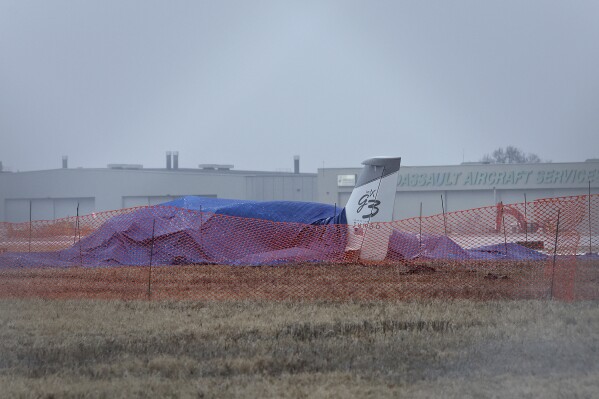 The wreckage of a single-engine Cirrus SR 22 aircraft is covered by a blue tarp near a runway at the Bill and Hillary Clinton National Airport on Monday, Jan. 22, 2024, after it crashed on Sunday in Little Rock, Ark. The pilot of the aircraft was pronounced dead at the scene and was the only individual on board at the time of the incident. (Colin Murphey /Arkansas Democrat-Gazette via AP)