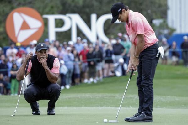 Tiger Woods, left, watches his son Charlie Woods, right, putt on the 18th green during the first round of the PNC Championship golf tournament Saturday, Dec. 17, 2022, in Orlando, Fla. (AP Photo/Kevin Kolczynski)