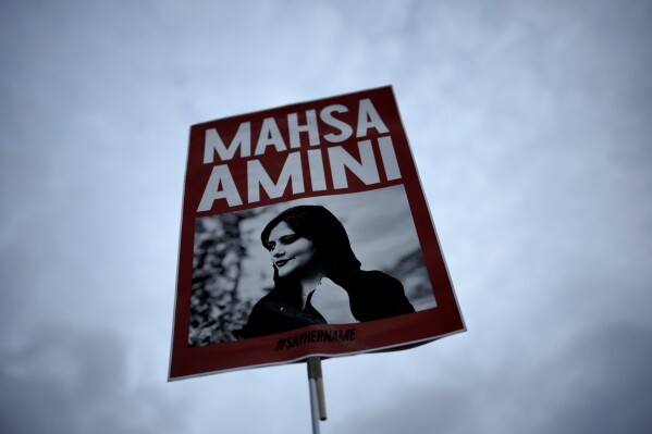 FILE - A woman holds a placard with a picture of Iranian woman Mahsa Amini during a protest against her death, in Berlin, Germany, on Sept. 28, 2022. Iran is responsible for the "physical violence" that led to the death of Mahsa Amini in September 2022 and sparked nationwide protests against the country's mandatory headscarf, or hijab, laws and its ruling theocracy, a U.N. fact-finding mission said Friday, March 8, 2024. (AP Photo/Markus Schreiber, File)