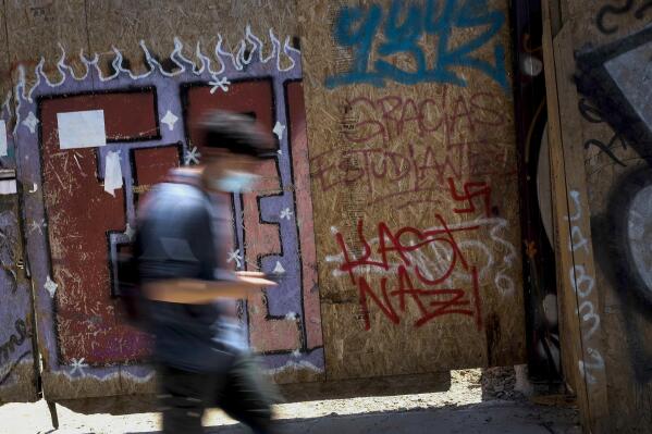 A youth walks past graffiti that reads "Kast, Nazi," referring to presidential candidate Jose Antonio Kast of the Republican Party, in Santiago, Chile, Tuesday, Dec. 7, 2021. (AP Photo/Matias Delacroix)