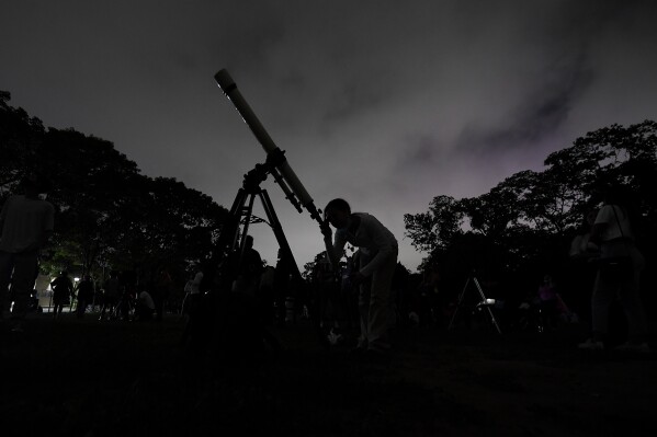 FILE - A girl looks at the moon through a telescope in Caracas, Venezuela, on Sunday, May 15, 2022. Six planets will line up in the early morning sky on June 3, 2024 but most won't be visible to the naked eye. A planetary parade happens relatively often when several planets align on the right side of the sun, making them visible across a narrow band of our sky. (AP Photo/Matias Delacroix)