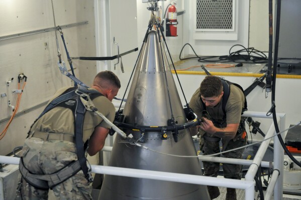 In this image provided by the U.S. Air Force, Senior Airman Jacob Deas, 23, left, and Airman 1st Class Jonathan Marrs, 21, right, secure the titanium shroud at the top of a Minuteman III intercontinental ballistic missile on Aug. 24, 2023, at the Bravo 9 silo at Malmstrom Air Force Base in Montana. After the shroud is secured, it is lifted off, revealing the black cone-shaped nuclear warhead inside. (John Turner/U.S. Air Force via AP)