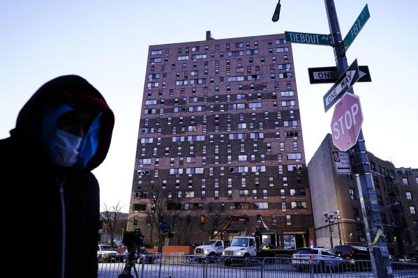 A person walks past an apartment building which suffered the city's deadliest fire in three decades, in the Bronx borough of New York, Tuesday, Jan. 11, 2022.  A malfunctioning electric space heater apparently started the fire Sunday in the 19-story building in the Bronx, fire officials said. (AP Photo/Matt Rourke)