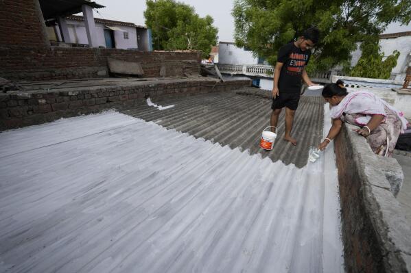 A resident of a shanty town helps her neighbour to paint his rooftop with cool white reflective paint which brings down indoor temperature in summer, in Ahmedabad, India, Monday, May 23, 2022. The intense heat wave sweeping through South Asia was made more likely due to climate change and it is a sign of things to come. An analysis by international scientists said that this heat wave was made 30-times more likely because of climate change, and future warming would make heat waves more common and hotter in the future. (AP Photo/Ajit Solanki)