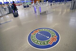 A traveler passes a sign recommending practicing social distancing, to limit spread of the coronavirus outbreak, at the nearly passenger-less JetBlue terminal at Logan Airport in Boston, Friday, May 29, 2020. (AP Photo/Charles Krupa)