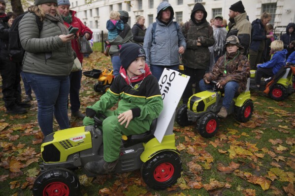 Seth James, left, and Eddie England, right, accompanied with their parents, attend a farmers protest to urge the government to change course over its inheritance tax plans, in London, Tuesday, Nov. 19, 2024. (AP Photo/Kin Cheung)