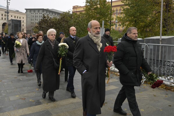 Employees of diplomatic missions walk to lay flowers at the monument, a large boulder from the Solovetsky islands, where the first camp of the Gulag political prison system was established, near the building of the Federal Security Service (FSB, Soviet KGB successor) in Lubyanskaya Square in Moscow, Russia, Sunday, Oct. 29, 2023. (AP Photo/Dmitry Serebryakov)
