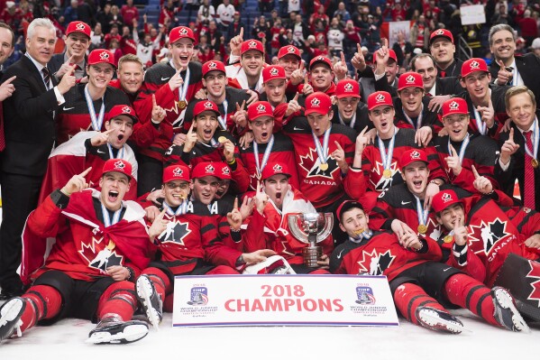 FILE - The Canadian team poses for a photo after winning the gold medal with a 3-1 win over Sweden during the third period the title game of the IIHF world junior hockey championships, Friday, Jan. 5, 2018, in Buffalo, N.Y. Five players from Canada's 2018 world junior team have taken a leave of absence from their respective clubs in recent days amid a report that five members of that team have been asked to surrender to police to face sexual assault charges. New Jersey’s Michael McLeod and Cal Foote, Philadelphia’s Carter Hart, Calgary’s Dillon Dube and former NHL player Alex Formenton have all been granted indefinite leave, with the absences announced this week. (Nathan Denette/The Canadian Press via AP, File)