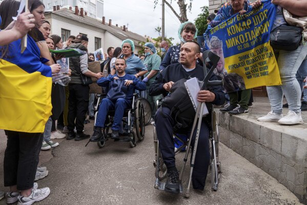 Injured Ukrainian soldiers ride on wheelchairs though human corridor with people holding photos of their missed relatives after returning from captivity during a POWs exchange between Russia and Ukraine, in Chernyhiv region, Ukraine, Saturday, May 24, 2025. (AP Photo/Evgeniy Maloletka)