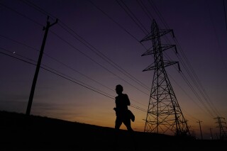 FILE - A jogger passes power lines during a sunset run, Aug. 20, 2023, in San Antonio, as high temperatures continue to stress the power grid. On Thursday, Sept. 7, Texas' power grid manager again asked residents to cut back on electricity as a prolonged and punishing summer heat wave continued, a day after the system was pushed to brink of outages for the first time since a deadly winter blackout in 2021. (AP Photo/Eric Gay, File)