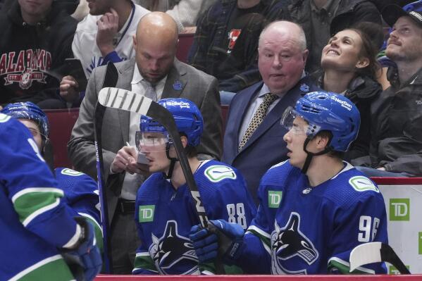 Vancouver Canucks head coach Bruce Boudreau, back right, and assistant coach Mike Yeo stand on the bench behind players Nils Aman (88), of Sweden, and Andrei Kuzmenko (96), of Russia, during the third period of an NHL hockey game against the Carolina Hurricanes in Vancouver, British Columbia,  Monday, Oct. 24, 2022. (Darryl Dyck/The Canadian Press via AP