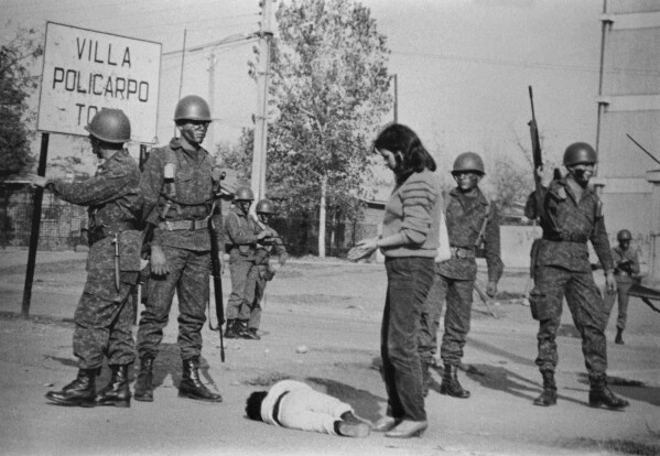 A woman's son lays on the ground crying after his father was arrested as soldiers carry out a military operation in the San Miguel area of Santiago, Chile, May 1986. (AP Photo/Marco Ugarte)