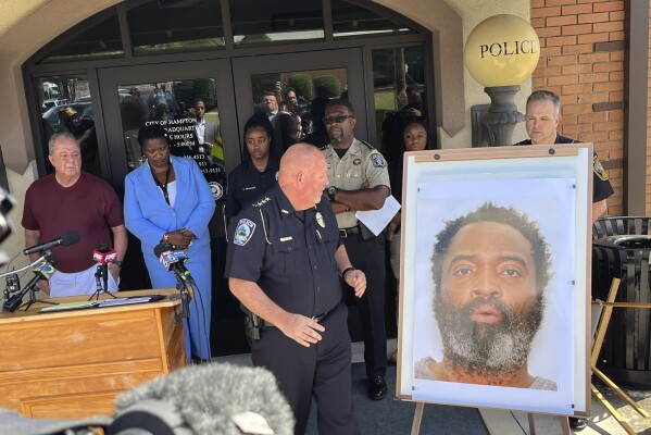 In this photo tweeted by WSB-TV's Steve Gehlbach, Hampton Police Chief James Turner, center, stands next to a mounted picture of suspect Andre Longmore during a news conference in Hampton, Ga., Saturday, July 15, 2023. Authorities are searching for Longmore, who is suspected of gunning down three men and a woman in Hampton. (Steve Gehlbach/WSB-TV via AP)