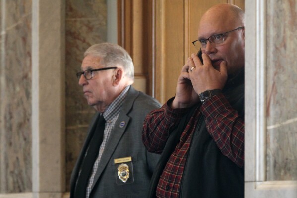 FILE - Kansas Republican Party Chairman Mike Brown, right, watches and works on his cell phone from the floor of the Kansas House, March 15, 2023, at the Statehouse in Topeka, Kan. Two top Kansas Republican Party officials, including Brown, are facing calls to resign over a viral online video showing people at a fundraiser kicking and beating a mannequin with a mask of President Joe Biden, highlighting the GOP's deep divisions and problems with suburban voters. (AP Photo/John Hanna, File)