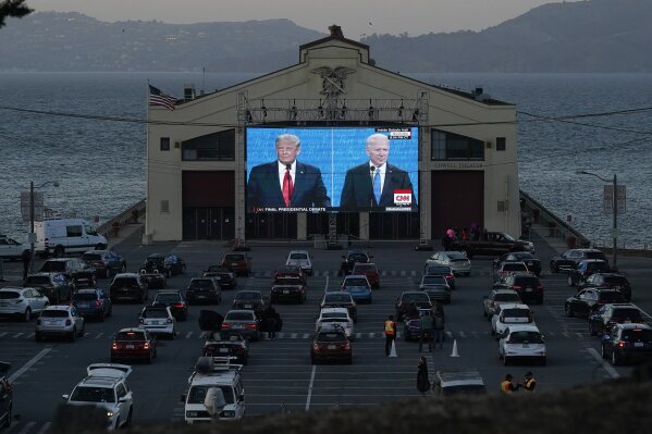 People watch from their vehicles as President Donald Trump, on left of video screen, and Democratic presidential candidate former Vice President Joe Biden speak during a Presidential Debate Watch Party at Fort Mason Center in San Francisco, Thursday, Oct. 22, 2020. The debate party was organized by Manny's, a San Francisco community meeting and learning place. (AP Photo/Jeff Chiu)