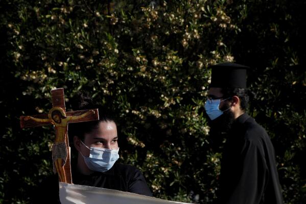 A female protestor holds a cross as an Orthodox priest passes during a protest against the Cyprus' song in Eurovision, outside Cyprus' national broadcasting building in capital Nicosia, Cyprus, Wednesday, May 19, 2021. Several dozen Orthodox Christian faithful including clergymen held up wooden crucifixes, icons of saints and a banner declaring Cyprus’ love for Christ in a renewed protest over Cyprus’ controversial entry for the Eurovision song contest that they contend promotes worship of Satan.  (AP Photo/Petros Karadjias)