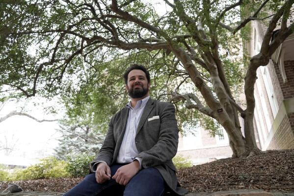 Benjamin Frey, American Studies professor at the University of North Carolina, sits under the native Ilex vomitoria tree on campus in Chapel Hill, N.C., Thursday, Feb. 24, 2022. Frey, a member of the Eastern Band of Cherokee Indians, led the language research behind a new smartphone interface by Lenovo-owned Motorola. The Cherokee language interface on its newest line of phones, uses the syllable-based written characters first created by the Cherokee Nation's Sequoyah in the early 1800s. (AP Photo/Gerry Broome)