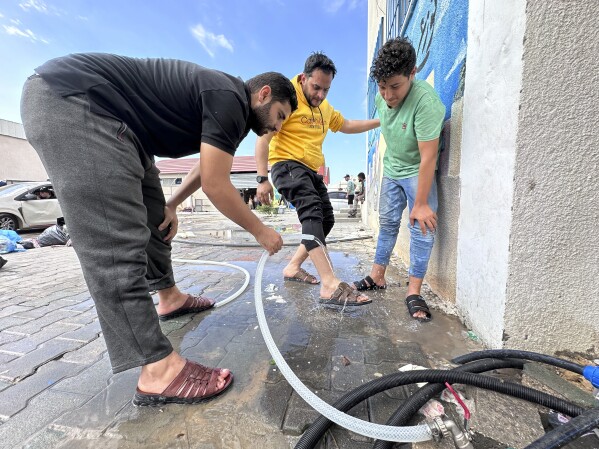 In this image provided by UNRWA, people use irrigation water to wash their feet at a shelter in southern Gaza on Monday Oct. 16, 2023. More than 2 million people, the majority of the Strip’s population, cram into what’s left. (Hosein Owda/UNRWA via AP)