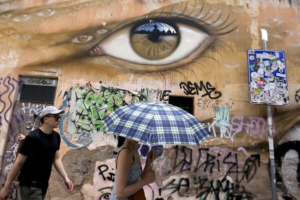 A woman uses an umbrella to take shelter from the sun as she walks in downtown Rome, Thursday, July 13, 2023. (AP Photo/Alessandra Tarantino)