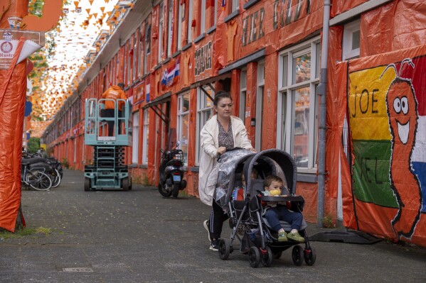 A woman walks past orange tarp, orange bunting, and Dutch national flags decorating Marktweg street in The Hague, Netherlands, Thursday June 13, 2024, one day ahead of the start of the Euro 2024 Soccer Championship. The Marktweg is one of several streets in the Netherlands that get an all-encompassing orange facelift during European Championships and World Cups when the national team, known as Oranje after the Dutch royal family and the color of their shirts, are playing. (AP Photo/Peter Dejong)