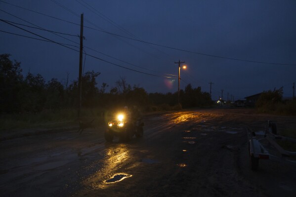 A villager rides an ATV vehicle along Main Street following evening rainfall, Sunday, Aug. 20, 2023, in Akiachak, Alaska. (AP Photo/Tom Brenner)