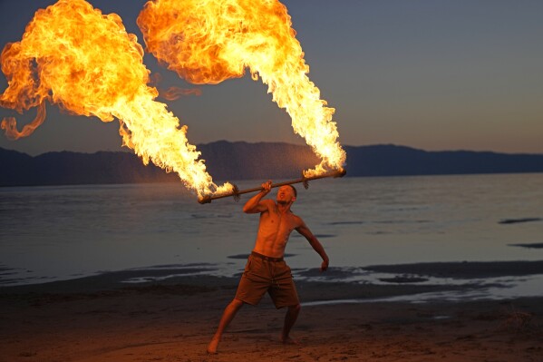 Tyler Oborn fire spins at a gathering of dancers and performers on the shoreline of the Great Salt Lake on June 15, 2023, in Magna, Utah. Oborn, who also works at a pontoon boat tour company, said the lake’s rise has given communities that rely on it new life. (AP Photo/Rick Bowmer)