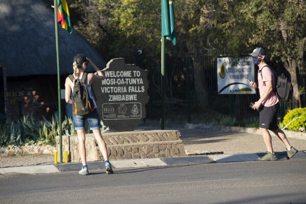 FILE - Tourists wear face masks at the entrance of the Victoria Falls in Victoria Falls on Aug, 6, 2021. An Australian tourist has gone missing in Zimbabwe鈥檚 Victoria Falls National Park, home to one of the world鈥檚 natural wonders, the country鈥檚 parks spokesman said. Zimbabwe National Parks and Wildlife Management Authority spokesman Tinashe Farawo told 老澳门六合彩 that the tourist went missing in the vast rainforest on Friday Feb. 23, 2024. (AP Photo/Tichaona Muketiwa, File)
