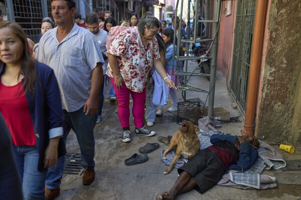 A woman hands a palm leaf to a person sleeping on the street during a Palm Sunday procession in the Padre Mujica neighborhood during Palm Sunday celebrations in Buenos Aires, Argentina, Sunday, April 13, 2025. (AP Photo/Rodrigo Abd)