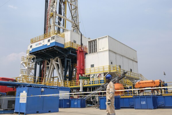 FILE - A Ugandan worker from China Oilfield Services Limited (COSL), a contractor for China National Offshore Oil Corporation (CNOOC), walks past the drilling rig at the Kingfisher oil field on the shores of Lake Albert in the Kikuube district of western Uganda, Jan. 24, 2023. Uganda National, which owns part of the Kingfisher project, was among companies whose plans for renewable energy were aimed primarily at using the clean power to decarbonize its fossil fuel projects, not replace them with cleaner pursuits. (AP Photo/Hajarah Nalwadda, File)