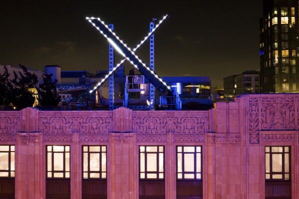 FILE - Workers install lighting on an "X" sign atop the company headquarters, formerly known as Twitter, in downtown San Francisco, Friday, July 28, 2023. Elon Musk’s social media platform formerly known as Twitter has sued the state of California over a law requiring social media companies to publish their policies for removing offending material such as hate speech, misinformation and harassment. (AP Photo/Noah Berger, File)