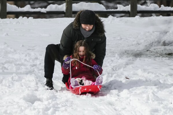 A woman plays with a child that is sledding in New York's Central Park Tuesday, Feb. 13, 2024. Technology glitches kept many New York City teachers and students from virtual classes Tuesday — the first attempt by the country's largest school system to switch to remote learning for a snow storm since the COVID-19 pandemic. (AP Photo/Frank Franklin II)