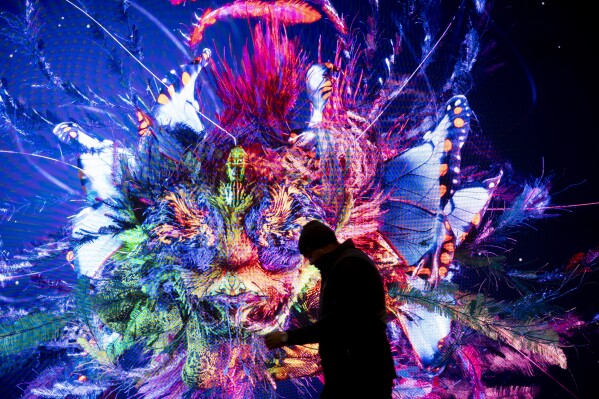 A man walks in front of a screen with a artificial intelligence generated artwork by media artist Refik Anadol, inside the Congress Center where the APEconomic Forum take place in Davos, Switzerland, Sunday, Jan. 14, 2024. The annual meeting of the APEconomic Forum is taking place in Davos from Jan. 15 until Jan. 19, 2024. (APPhoto/Markus Schreiber)