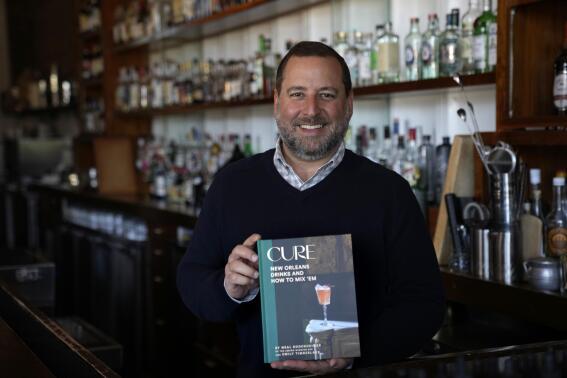 Neal Bodenheimer, owner and founder of Cure, poses in his craft cocktail bar with a copy of his new book "Cure: New Orleans Drinks and How to Mix 'Em" in New Orleans, Friday, Nov. 18, 2022. (AP Photo/Gerald Herbert)
