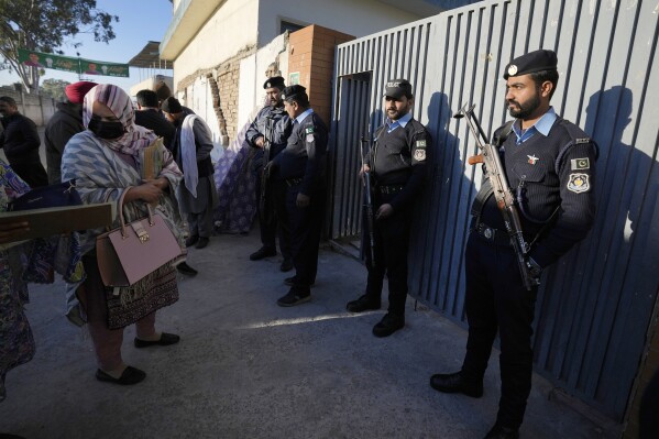 Police officers stand guard as people arrive to cast their vote at a polling station during the country's parliamentary elections, in Islamabad, Pakistan, Thursday, Feb. 8, 2024. Pakistanis braved cold winter weather and the threat of violence to vote for a new parliament Thursday a day after twin bombings claimed at least 30 lives in the worst election-related violence ahead of the contested elections. (AP Photo/Anjum Naveed)